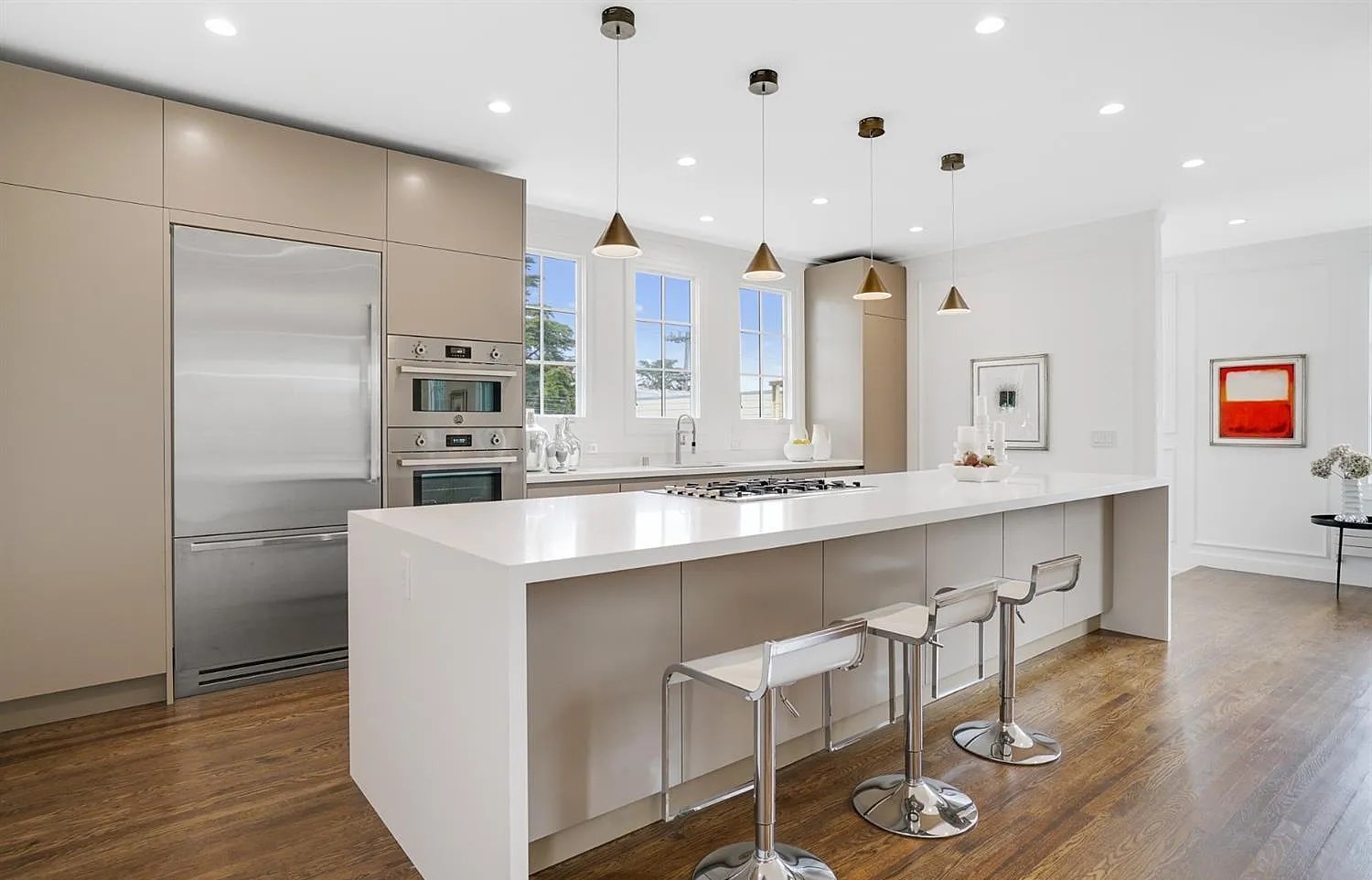 The finished kitchen: pale cabinetry, a long island, brass pendants.